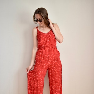 Puede incluir: Mono rojo con lunares blancos. El mono presenta un cuello en V, tirantes finos y cintura ceñida. Los pantalones capri se combinan con tacones negros. Un atuendo elegante para un evento informal o semiformal.