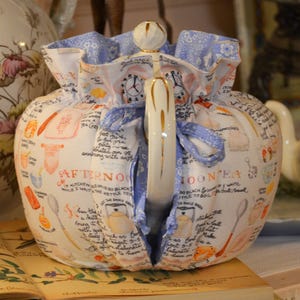 Może przedstawiać: Biały ceramiczny kubek z czarnym uchwytem i napisem "But First, Coffee" czarną, pogrubioną czcionką. Kubek stoi na drewnianej powierzchni.