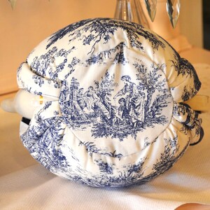 Op de afbeelding: Een wit en blauw toile de Jouy wijnfleshoes. De stof heeft een pastorale sc&egrave;ne met figuren en bomen. De hoes is om een fles gewikkeld, waarbij een deel van de hals zichtbaar is.