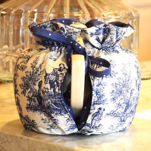 Op de afbeelding: Een wit en blauw toilettasje met een blauw lint. De tas heeft een klassiek toile-patroon met figuren en bomen. Een wit rechthoekig object is zichtbaar in de tas.
