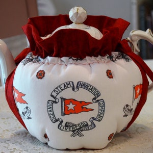 Puede incluir: Tetera blanca con una cubierta de tela roja. La cubierta tiene un logotipo azul marino que dice "Oceanic Steam Navigation Company Liverpool" con una estrella roja y una bandera roja.