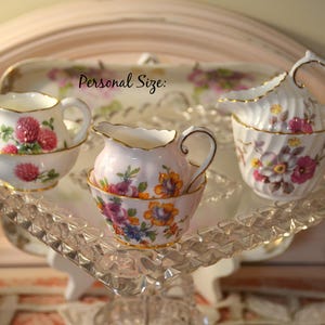 May include: Three white porcelain creamers and sugar bowls with gold rims and floral patterns, including red clover and mixed blossoms. The text "Personal Size:" is visible above the items, which are arranged on a clear, textured glass tray.