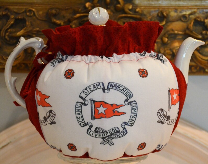 Puede incluir: Tetera blanca con un calienta-te rojo y blanco. El calienta-te tiene un volante rojo y presenta una estrella blanca sobre una bandera roja con el texto "Oceanic Steam Navigation Company Liverpool" en un c&iacute;rculo.