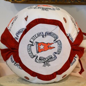 Puede incluir: Una bola de tela blanca y roja con una cinta roja y un c&iacute;rculo blanco con el texto "Oceanic Steam Navigation Company Liverpool" en negro.