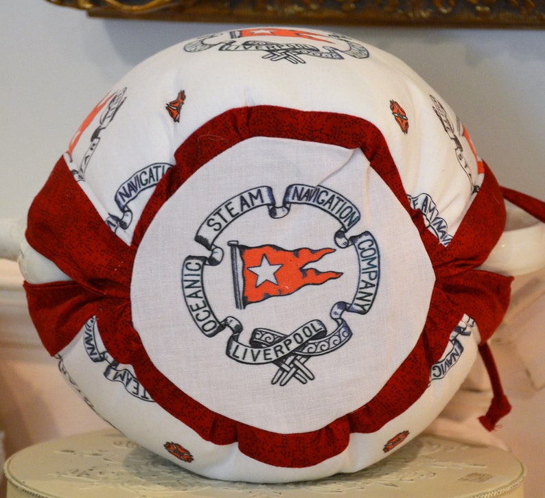 Puede incluir: Una bola de tela blanca y roja con una cinta roja y un c&iacute;rculo blanco con el texto "Oceanic Steam Navigation Company Liverpool" en negro.