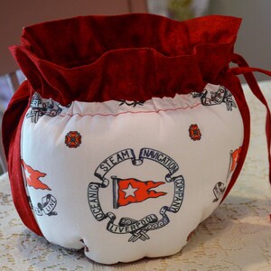 Puede incluir: Bolsa de tela roja con cord&oacute;n de ajuste y forro de tela blanca. La bolsa tiene un dise&ntilde;o impreso de una bandera de barco con el texto "Oceanic Steam Navigation Company Liverpool" y una estrella roja.