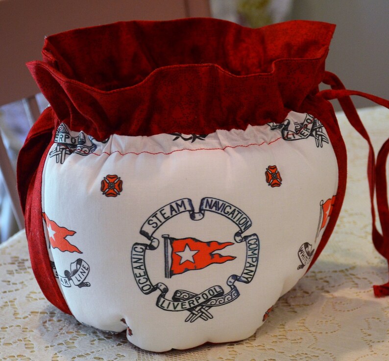 Puede incluir: Bolsa de tela roja con cord&oacute;n de ajuste y forro de tela blanca. La bolsa tiene un dise&ntilde;o impreso de una bandera de barco con el texto "Oceanic Steam Navigation Company Liverpool" y una estrella roja.