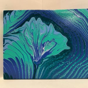 May include: Abstract acrylic painting on canvas with a fluid art design. The artwork features a blend of teal, turquoise, and navy blue hues, creating a swirling, marbled effect. The composition includes a central, flower-like shape.