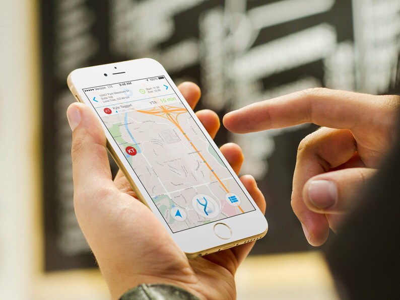 以下が含まれることがあります： 人がスマートフォンを使って地図アプリでナビゲートしています。画面には、青いルートと「KT」というラベルの付いた赤いマーカーが表示された地図が表示されています。アプリは、到着予定時刻を「15分」と表示しています。