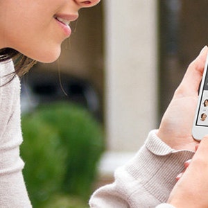 以下が含まれることがあります： スマートフォンを使ってカレンダーアプリを見ている人がいます。アプリは3月のカレンダーを表示しており、27日に青い点が付いています。アプリは、名前と時間付きのスケジュールされた予定のリストも表示しています。