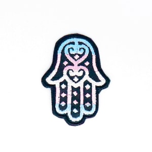 May include: A black embroidered patch with a hamsa hand design. The hamsa is filled with a blue, pink, and white color pattern.