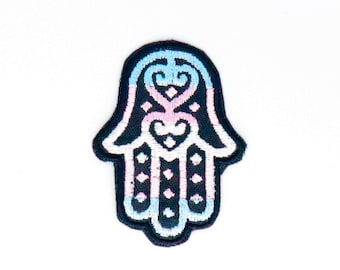 May include: A black embroidered patch with a hamsa hand design. The hamsa is filled with a blue, pink, and white color pattern.