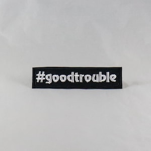 Puede incluir: Parche bordado negro con texto blanco que dice "#goodtrouble".