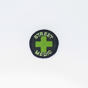 May include: A black and green embroidered patch with the text "STREET MEDIC" and a green cross in the center.