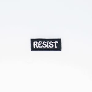 May include: Black fabric patch with white embroidered text that reads "RESIST".