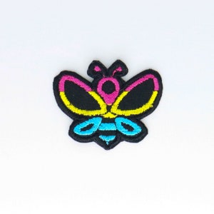 May include: A black embroidered bee patch with yellow, pink and blue accents. The bee is stylised with a simple design and is a popular symbol of the LGBTQ+ community.