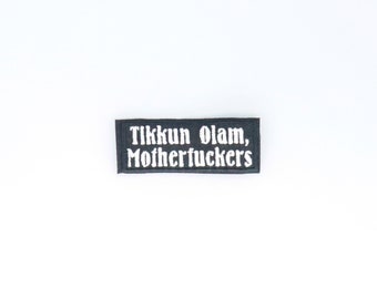 May include: Black rectangular patch with white text that reads "Tikkun Olam, Motherfuckers".