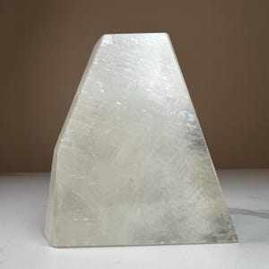 May include: A large, clear, crystal pyramid with a smooth, polished surface. The pyramid is made of selenite, a type of gypsum.