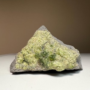 May include: A rough-hewn rock formation with a gray base and a vibrant, lime-green crystalline surface. The stone has a natural, irregular shape, showcasing a mix of textures and colors, perfect for collectors or decorative use.