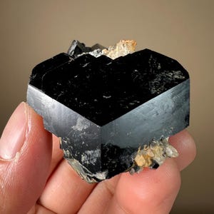 May include: A black, multifaceted, geometrically shaped crystal with a sharp, pointed top. The crystal is surrounded by smaller, white crystals.
