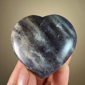 May include: A heart-shaped polished stone with a swirling pattern of grey, white, and black. The stone has a smooth, polished surface.