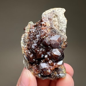 May include: A white ceramic mug with a black handle and the text "But First, Coffee" in a bold, black font. The mug is set against a blurred background, suggesting a cozy setting.