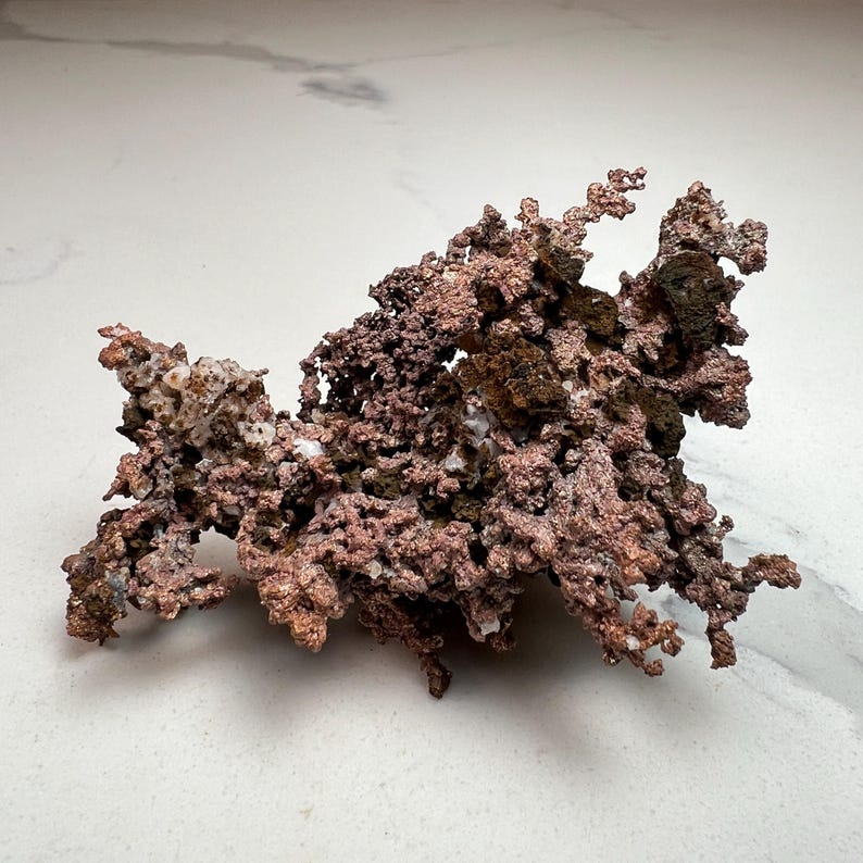 Pode incluir: Um esp&eacute;cime de cobre natural com uma estrutura ramificada complexa. A pe&ccedil;a exibe uma gama de cores, do castanho-avermelhado brilhante a tons mais escuros, quase pretos. A superf&iacute;cie tem uma apar&ecirc;ncia &aacute;spera e texturizada, com pequenas forma&ccedil;&otilde;es cristalinas.