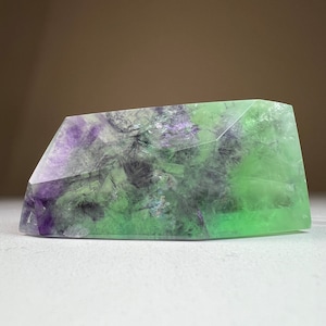 May include: A large, green and purple fluorite crystal with a geometric shape. The crystal is translucent and has a variety of shades of green and purple.