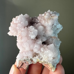 May include: A cluster of pale pink quartz crystals with a rough, natural base. The crystals are clustered together in a dense formation, creating a unique and interesting texture.