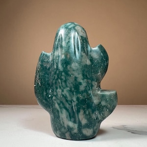 May include: A green and white marble cactus sculpture. The stone sculpture has a smooth, polished surface with a natural pattern of green and white veining. The cactus shape has a rounded top and several side arms, creating a unique decorative piece.