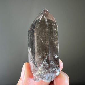 May include: A clear quartz crystal with inclusions of black tourmaline. The crystal is a double terminated point with a natural, rough surface.