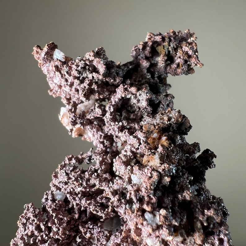 Pode incluir: Close-up de um esp&eacute;cime mineral de cobre com uma superf&iacute;cie &aacute;spera e texturizada. O mineral tem uma mistura de cores castanho-avermelhadas e castanho-escuras, com pequenas inclus&otilde;es de cristais brancos. A forma geral &eacute; irregular e irregular.