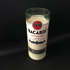 May include: A white candle in a clear glass bottle with a Bacardi Superior label. The label features a black bat logo and the text "Bacardi Superior Ron Superior Carta Blanca".