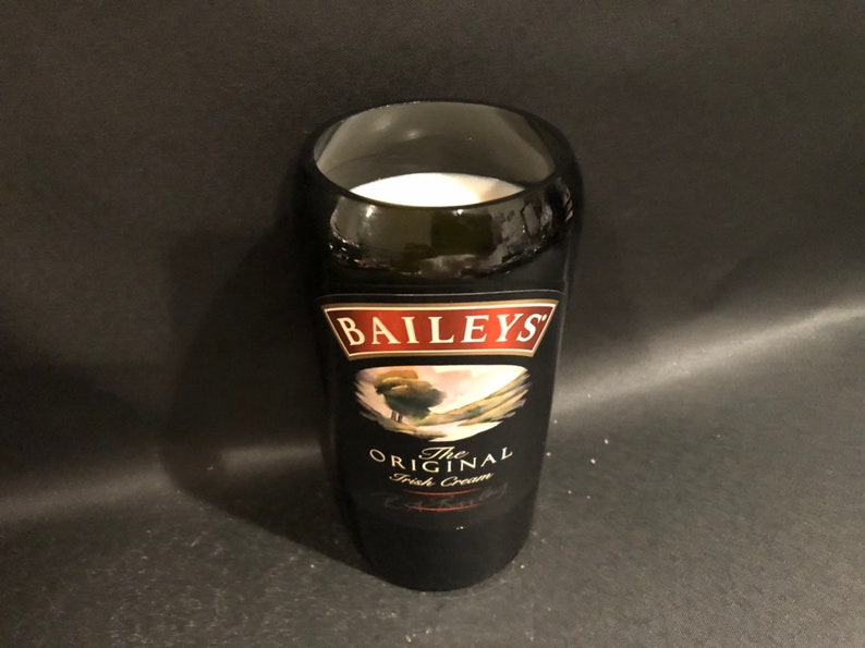 May include: A black glass with the label of Baileys The Original Irish Cream. The glass is filled with a white liquid. The label features the Baileys logo and a landscape scene.