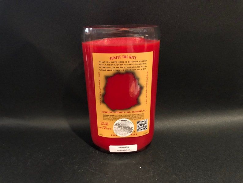 May include: A red glass candle jar with a gold label that reads "Ignite the Nite" and "Cinnamon". The label also includes the text "What you have here is smooth whiskey with a fiery kick of red hot cinnamon. It tastes like heaven, burns like hell. What happens next is up to you."