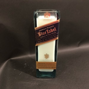 May include: A rectangular glass bottle with a blue and gold label reading "Johnnie Walker Blue Label Blended Scotch Whisky." The bottle has a white interior. The background is dark.