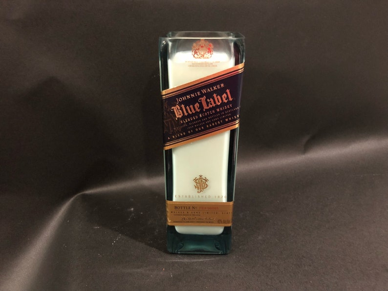 May include: A rectangular glass bottle with a blue and gold label reading "Johnnie Walker Blue Label Blended Scotch Whisky." The bottle has a white interior. The background is dark.