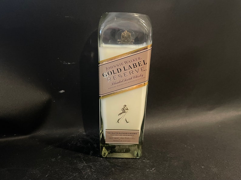 May include: A clear glass candle in the shape of a Johnnie Walker Gold Label Reserve whisky bottle. The label is gold with black text and a walking man logo.