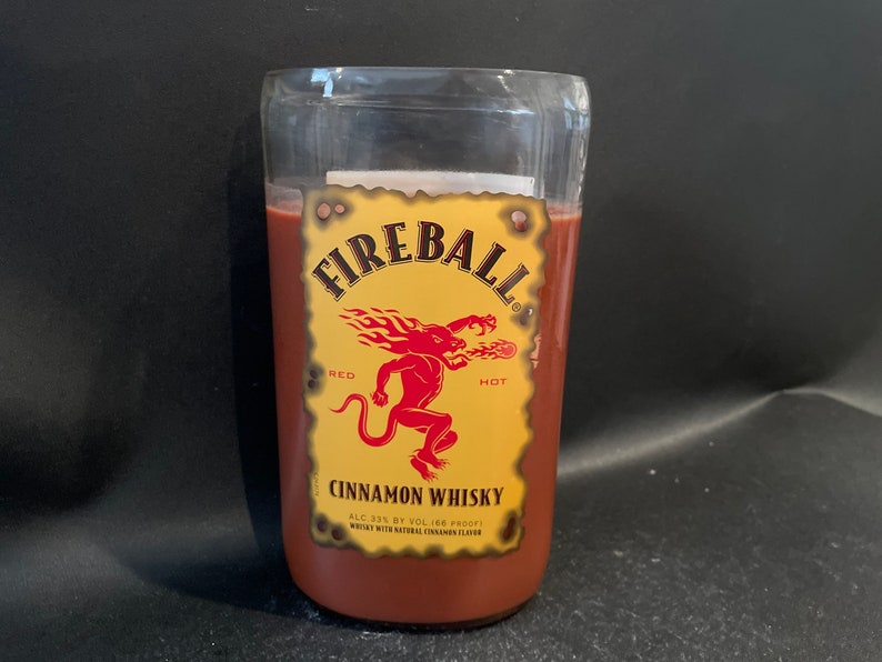 May include: A glass bottle with a red liquid inside. The bottle has a yellow label with the words "Fireball", "Red", "Hot", "Cinnamon Whisky", "ALC 33% BY VOL 166 PROOF", and "WHISKEY WITH NATURAL CINNAMON FLAVOR".