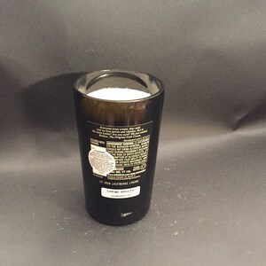May include: A dark brown glass filled with a white substance, possibly a beverage or dessert. The glass has a label with text and a white sticker. The product is labeled "CREME BRULEE".
