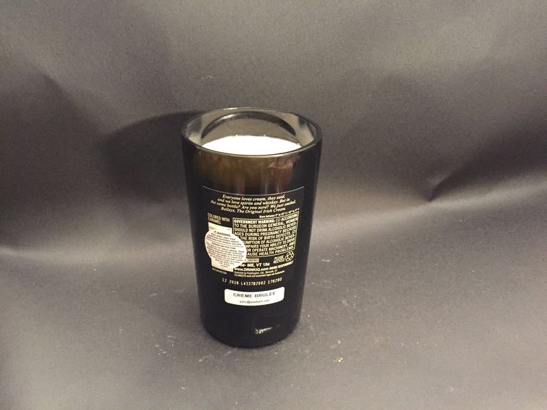May include: A dark brown glass filled with a white substance, possibly a beverage or dessert. The glass has a label with text and a white sticker. The product is labeled "CREME BRULEE".