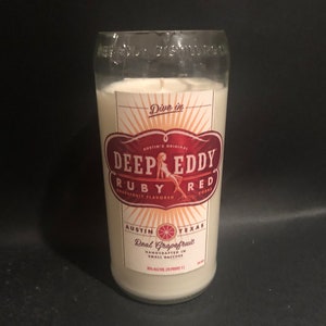 May include: A clear glass bottle candle with a white label. The label has a red and white design with the text "Deep Eddy Ruby Red Grapefruit Flavored Vodka".