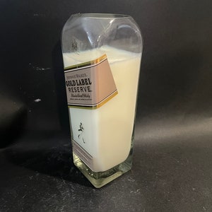 May include: A white candle in a clear glass bottle with a gold label that reads "Johnnie Walker Gold Label Reserve Blended Scotch Whisky".