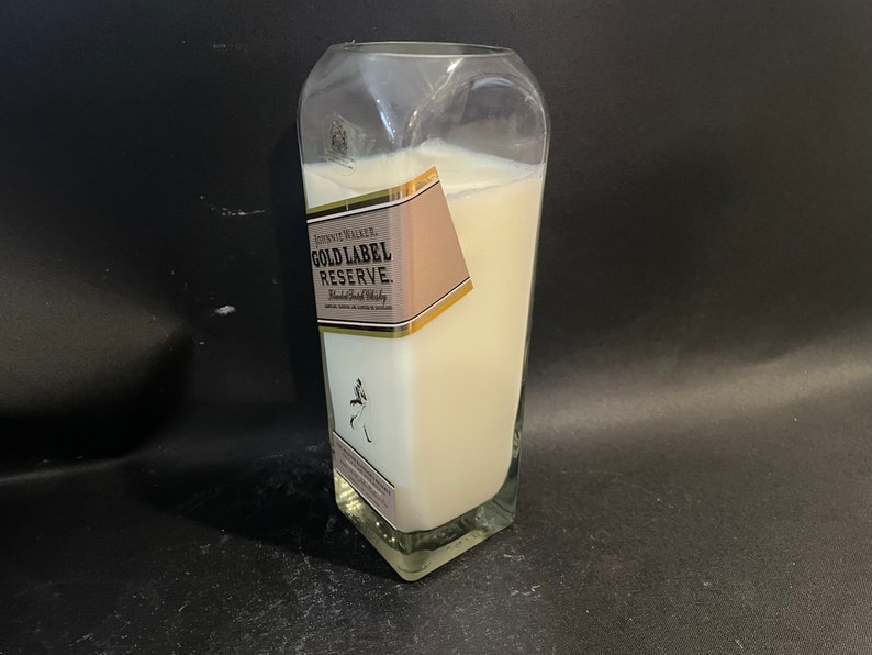 May include: A white candle in a clear glass bottle with a gold label that reads "Johnnie Walker Gold Label Reserve Blended Scotch Whisky".