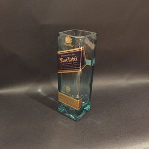 May include: A repurposed Johnnie Walker Blue Label bottle, now a vase. The clear glass vessel features the original label with gold and navy blue details. The square shape and label are clearly visible. A unique upcycled item.