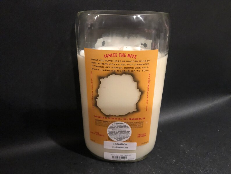 May include: A clear glass bottle candle with a white label that reads "Ignite the Nite" and "What you have here is smooth whisky with a fiery kick of red hot cinnamon. It tastes like heaven, burns like hell. What happens next is up to you." The label also includes the text "Cinnamon" and "info@fireballwhisky.com".