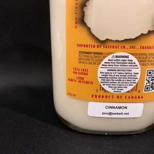 May include: A yellow and white candle jar with a cinnamon scent. The jar has a black label with the text "Cinnamon" and "pnc@swbell.net". The jar also has a yellow label with the text "Product of Canada" and a warning label with instructions for burning the candle safely.