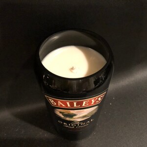 May include: A black glass candle holder with a white candle inside. The candle holder has a label that says "Baileys Original Irish Cream". The candle has a wooden wick.