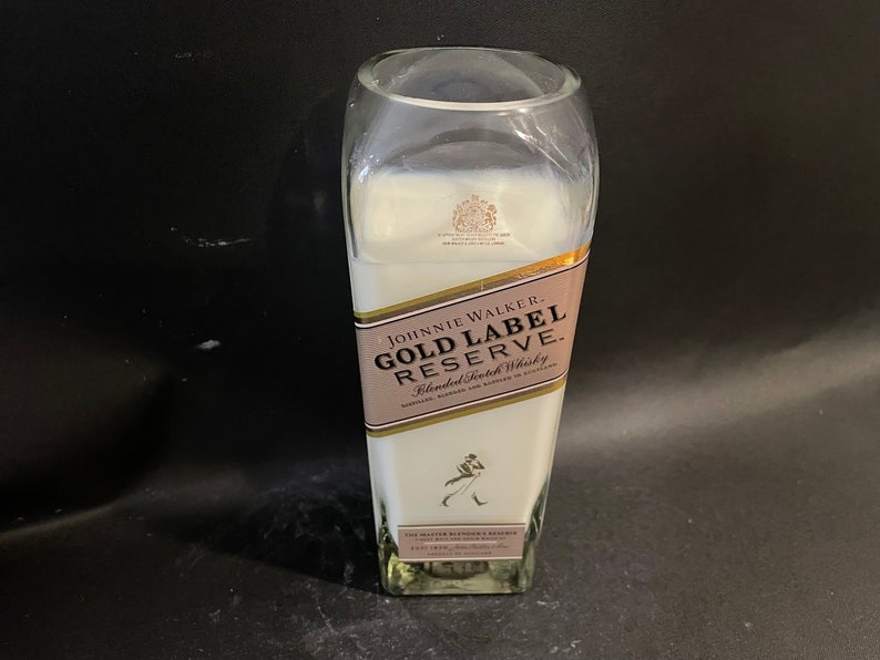 May include: A white candle in a clear glass bottle with a gold label that reads "JOHNNIE WALKER GOLD LABEL RESERVE Blended Scotch Whisky".