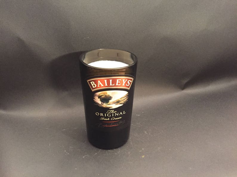 May include: A tall, dark glass with the Baileys Irish Cream logo, filled with a white liquid. The glass has a black and brown color scheme, with the Baileys logo prominently displayed. The glass is set against a dark background.